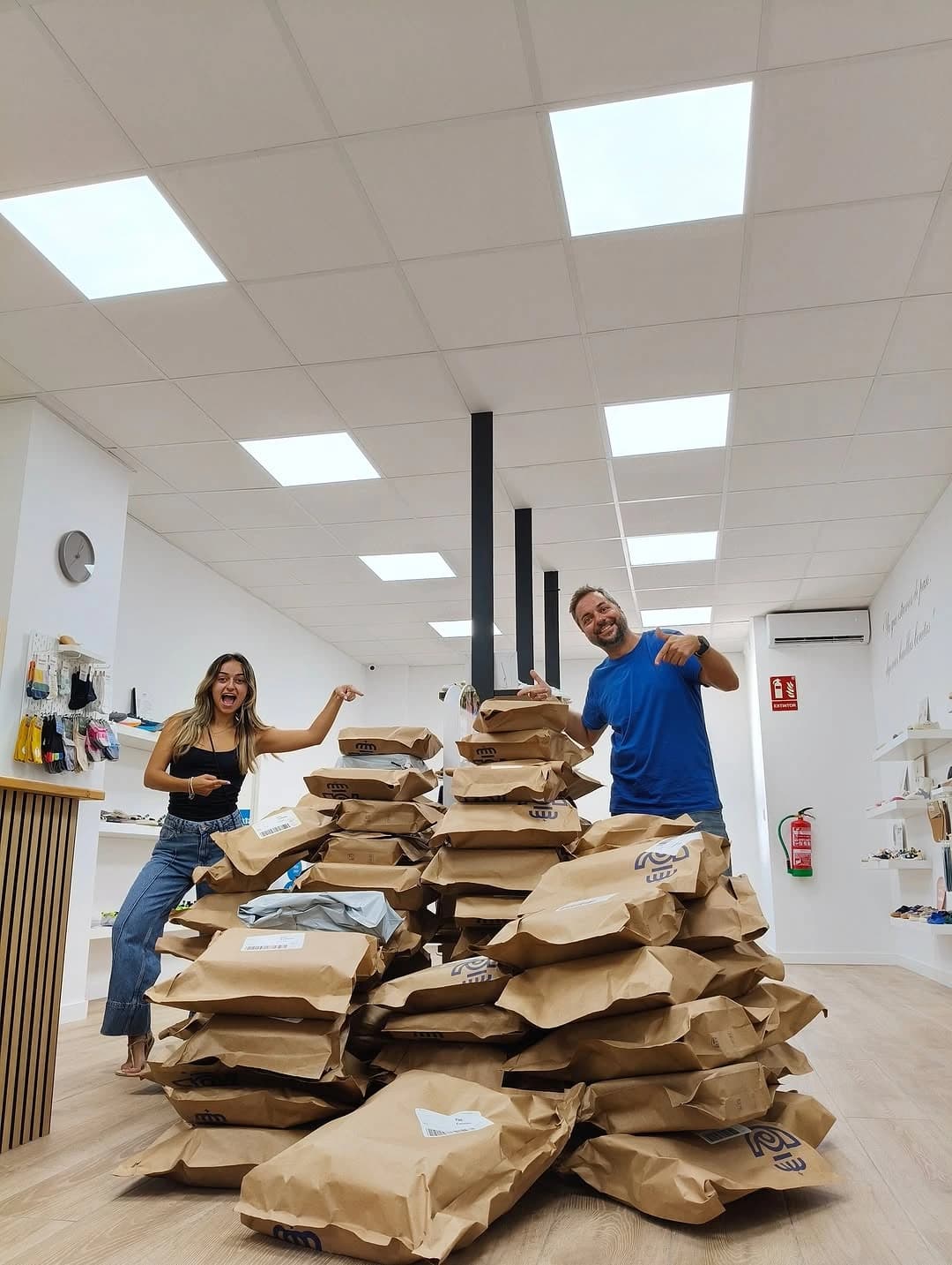 Two Kukinos team members smiling next to a large pile of packaged orders, representing logistics success.